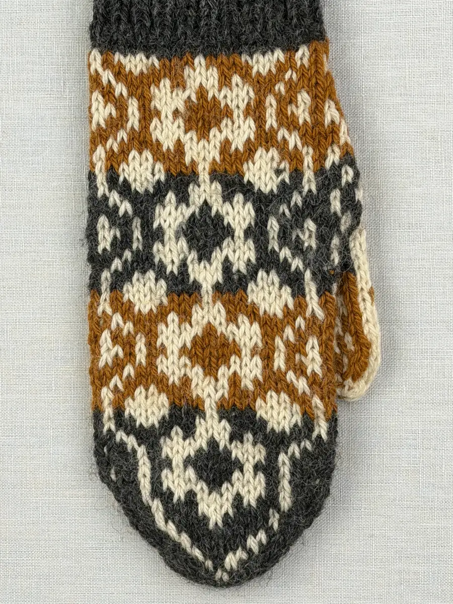 En stickad tumvante, med randig mudd i 1-1 resår (1 rät och 1 avig maska) och mönsterstickad vante i slätstickning, av 3-trådigt ullgarn.