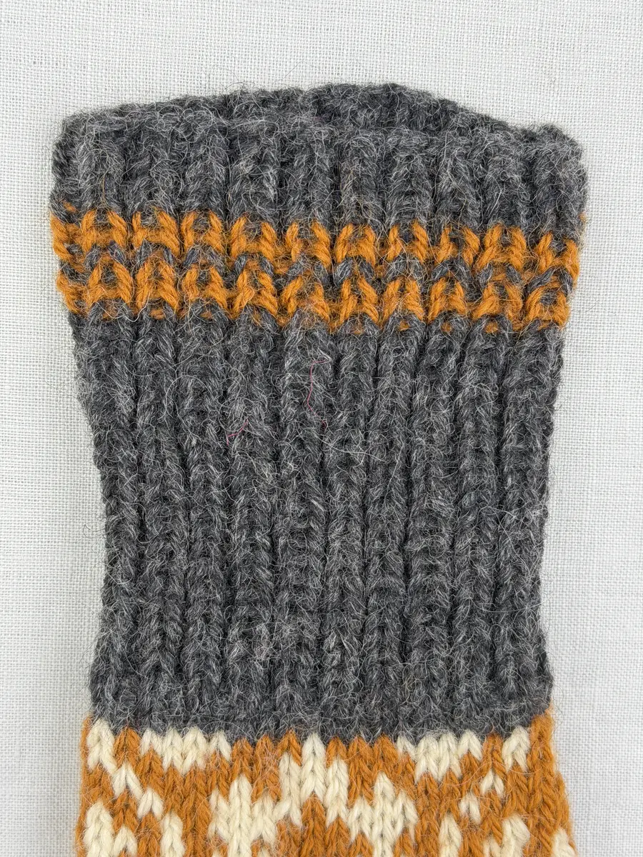 En stickad tumvante, med randig mudd i 1-1 resår (1 rät och 1 avig maska) och mönsterstickad vante i slätstickning, av 3-trådigt ullgarn.