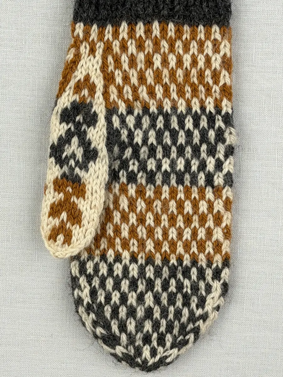 En stickad tumvante, med randig mudd i 1-1 resår (1 rät och 1 avig maska) och mönsterstickad vante i slätstickning, av 3-trådigt ullgarn.