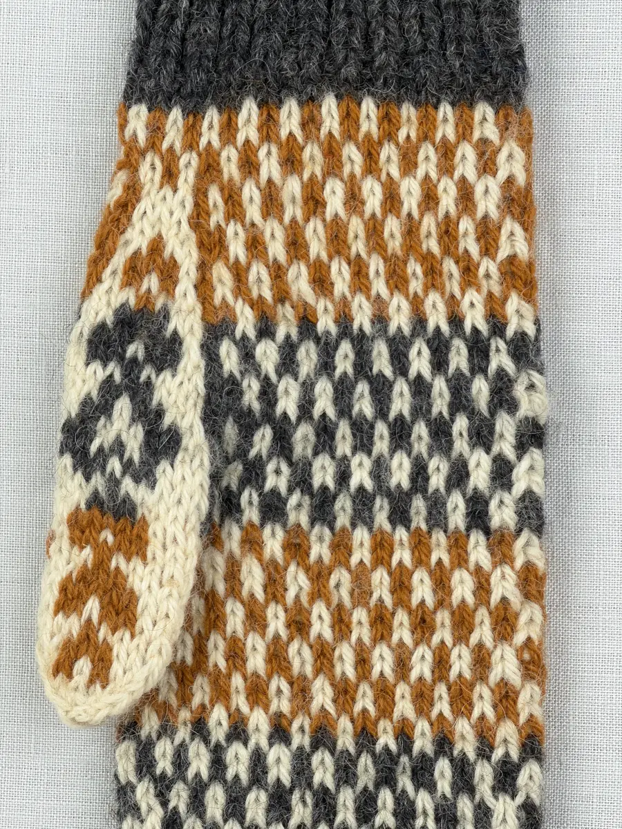 En stickad tumvante, med randig mudd i 1-1 resår (1 rät och 1 avig maska) och mönsterstickad vante i slätstickning, av 3-trådigt ullgarn.