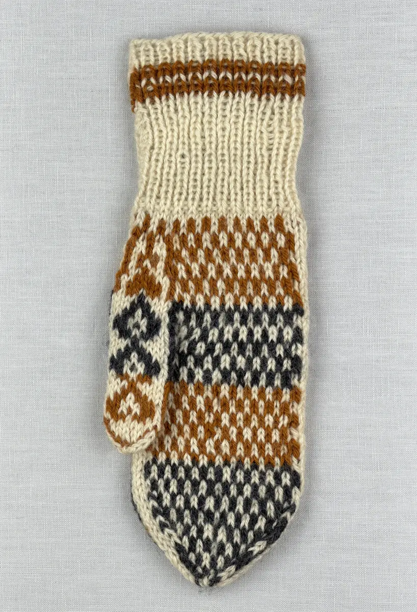 En stickad tumvante, med randig mudd i 1-1 resår (1 rät och 1 avig maska) och mönsterstickad vante i slätstickning, av 3-trådigt ullgarn.