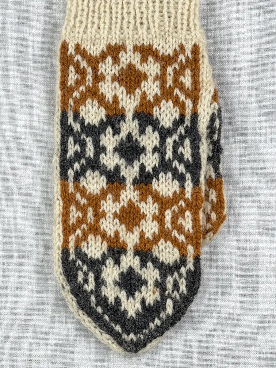 En stickad tumvante, med randig mudd i 1-1 resår (1 rät och 1 avig maska) och mönsterstickad vante i slätstickning, av 3-trådigt ullgarn.