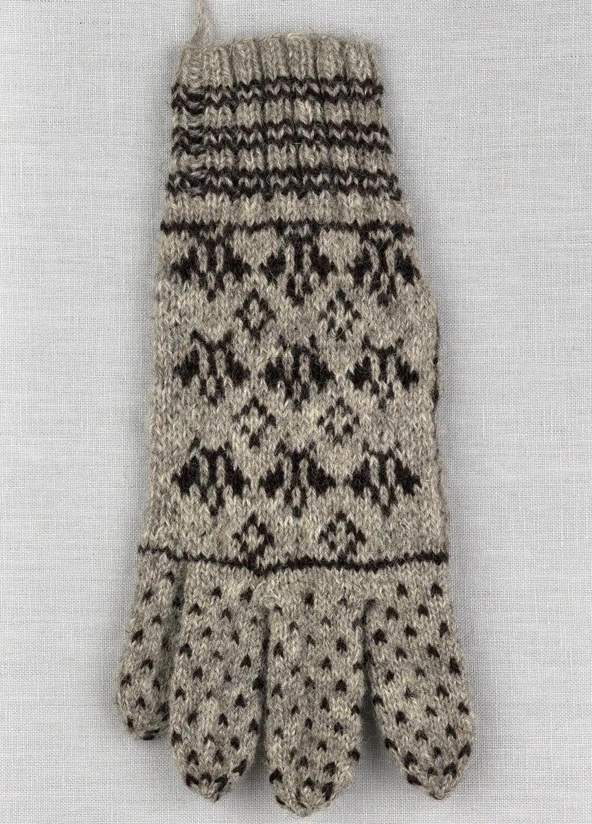 En stickad fingervante, med randig mudd i 2-2 resår (2 räta och 2 aviga maskor) och mönsterstickad vante i slätstickning, av 2-trådigt ullgarn.