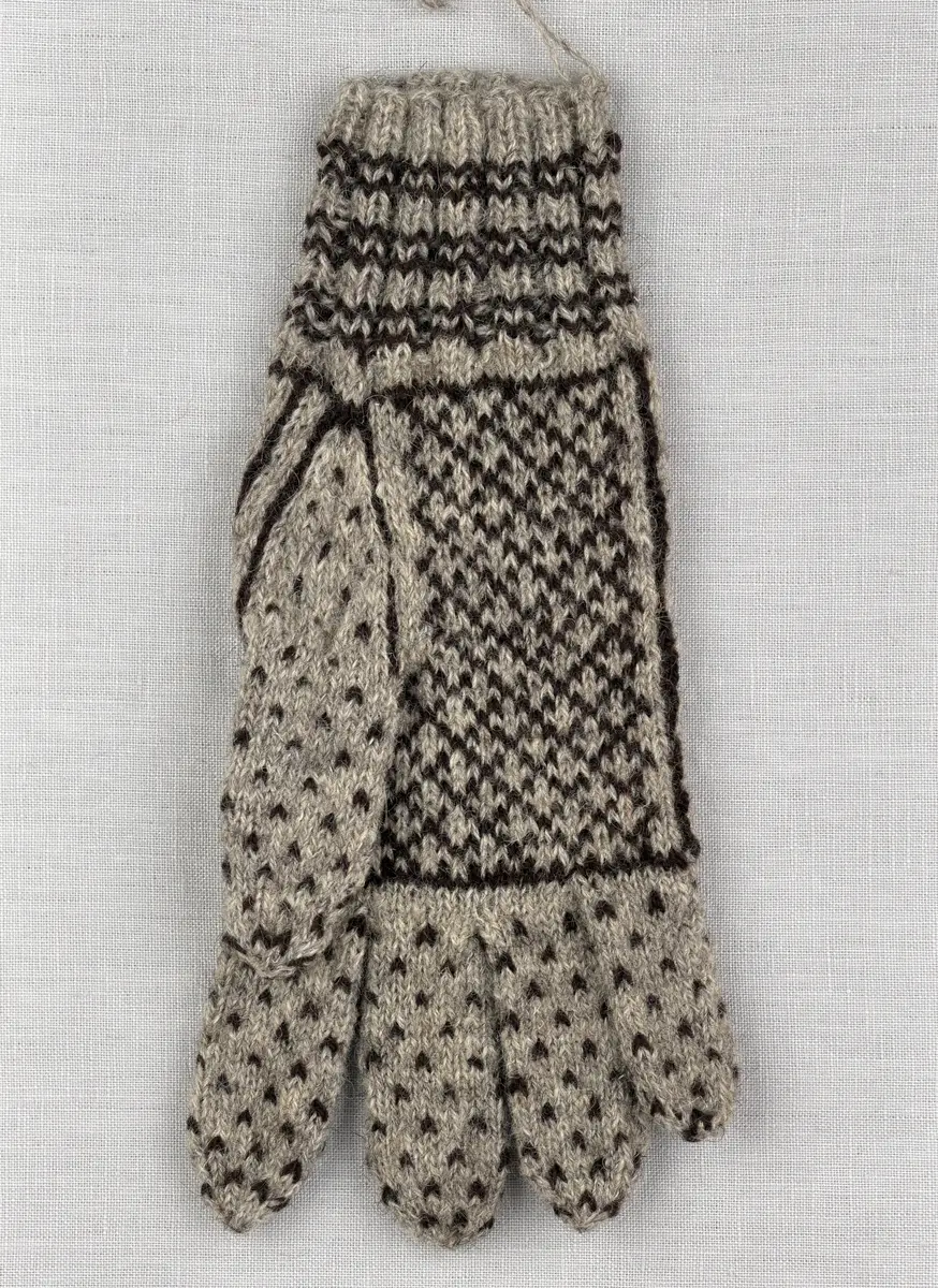 En stickad fingervante, med randig mudd i 2-2 resår (2 räta och 2 aviga maskor) och mönsterstickad vante i slätstickning, av 2-trådigt ullgarn.