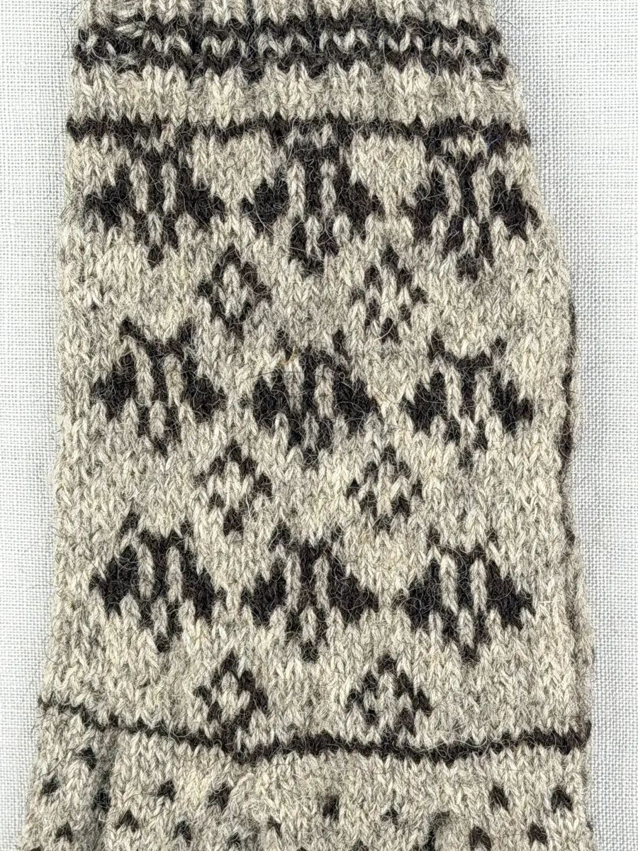 En stickad fingervante, med randig mudd i 2-2 resår (2 räta och 2 aviga maskor) och mönsterstickad vante i slätstickning, av 2-trådigt ullgarn.