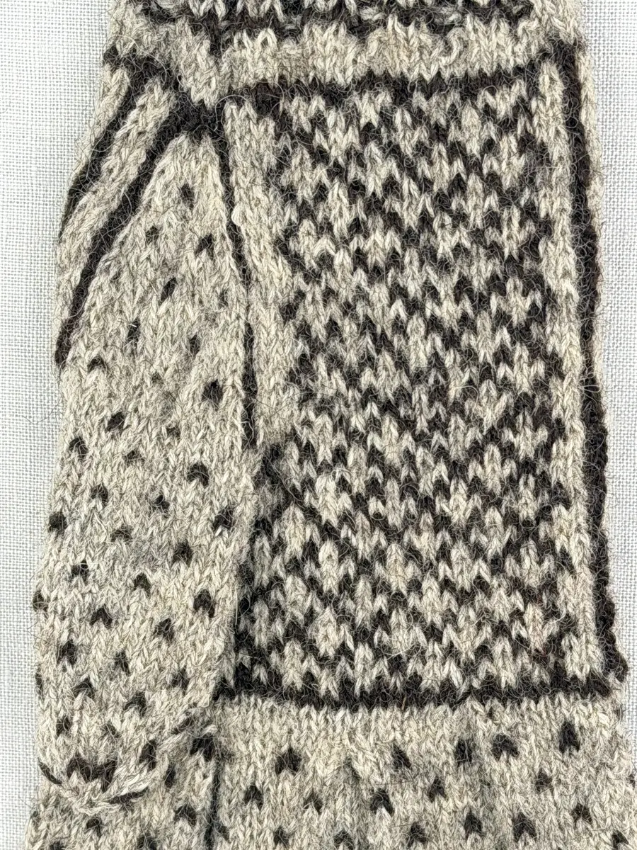 En stickad fingervante, med randig mudd i 2-2 resår (2 räta och 2 aviga maskor) och mönsterstickad vante i slätstickning, av 2-trådigt ullgarn.