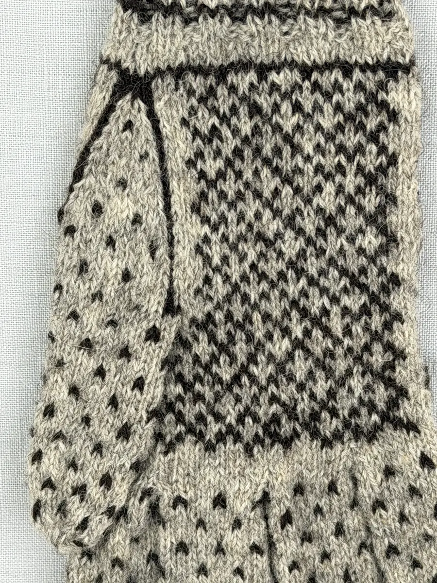 En stickad fingervante, med randig mudd i 2-2 resår (2 räta och 2 aviga maskor) och mönsterstickad vante i slätstickning, av 2-trådigt ullgarn. Framsidan är dekorerad med ett motiv föreställande Värmlandsgripen.