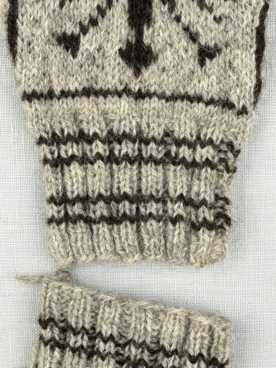 En stickad fingervante, med randig mudd i 2-2 resår (2 räta och 2 aviga maskor) och mönsterstickad vante i slätstickning, av 2-trådigt ullgarn. Framsidan är dekorerad med ett motiv föreställande Värmlandsgripen.