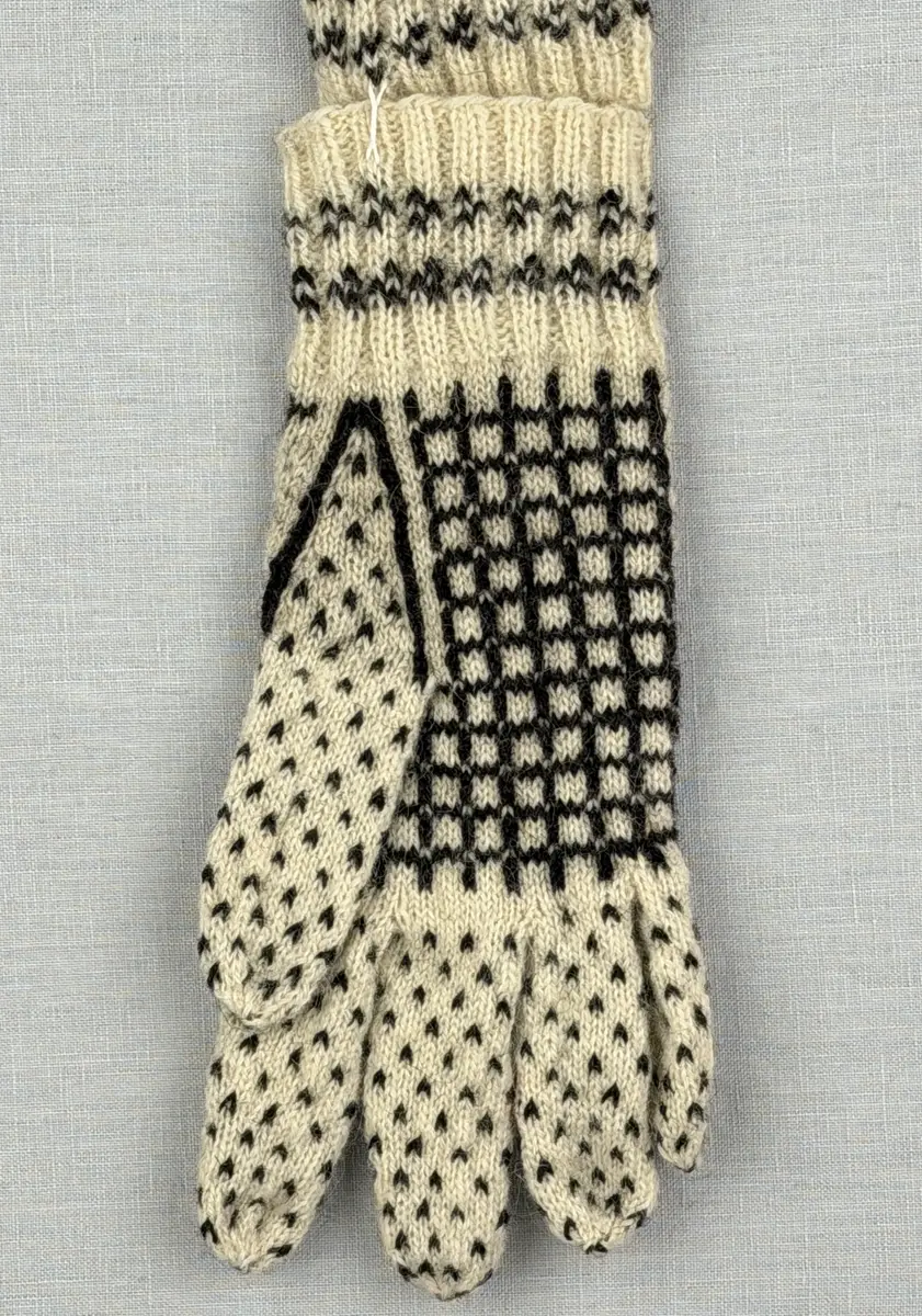 En stickad fingervante, med mönstrad mudd i 2-2 resår (2 räta och 2 aviga maskor) och mönsterstickad vante i slätstickning och aviga maskor, av 2-trådigt ullgarn. Framsidan är dekorerad med ett motiv föreställande Nils Holgerson sittande på en flygande gås.