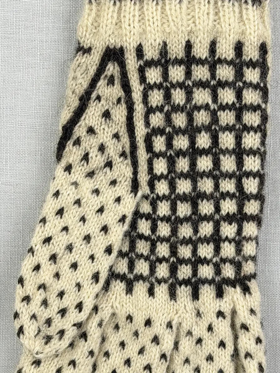 En stickad fingervante, med mönstrad mudd i 2-2 resår (2 räta och 2 aviga maskor) och mönsterstickad vante i slätstickning och aviga maskor, av 2-trådigt ullgarn. Framsidan är dekorerad med ett motiv föreställande Nils Holgerson sittande på en flygande gås.