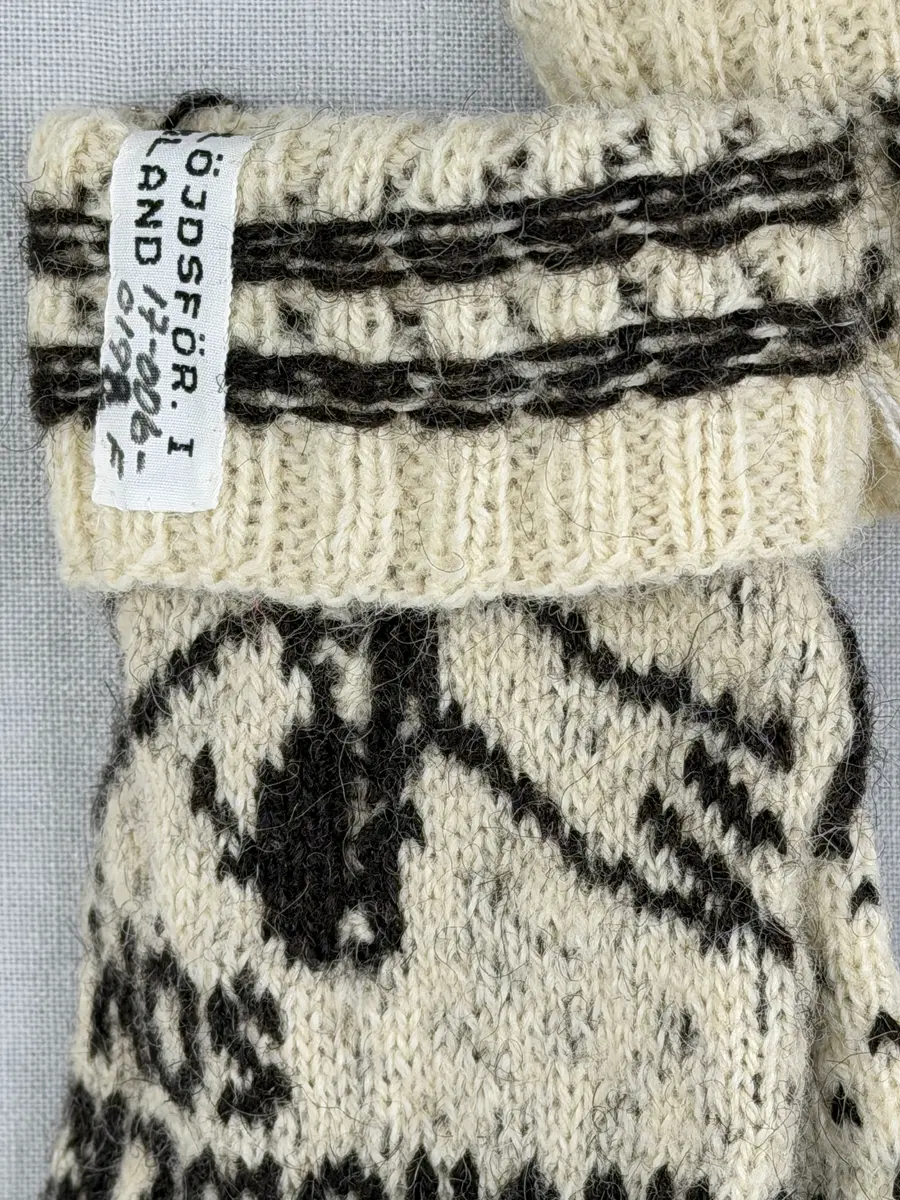 En stickad fingervante, med mönstrad mudd i 2-2 resår (2 räta och 2 aviga maskor) och mönsterstickad vante i slätstickning och aviga maskor, av 2-trådigt ullgarn. Framsidan är dekorerad med ett motiv föreställande Nils Holgerson sittande på en flygande gås.