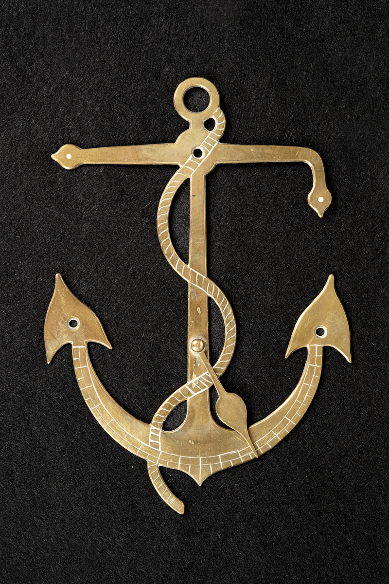 Regulator av mässing i form av ett ankare. Tillverkad i Reval av en maskinist ombord på FREJA 1888.