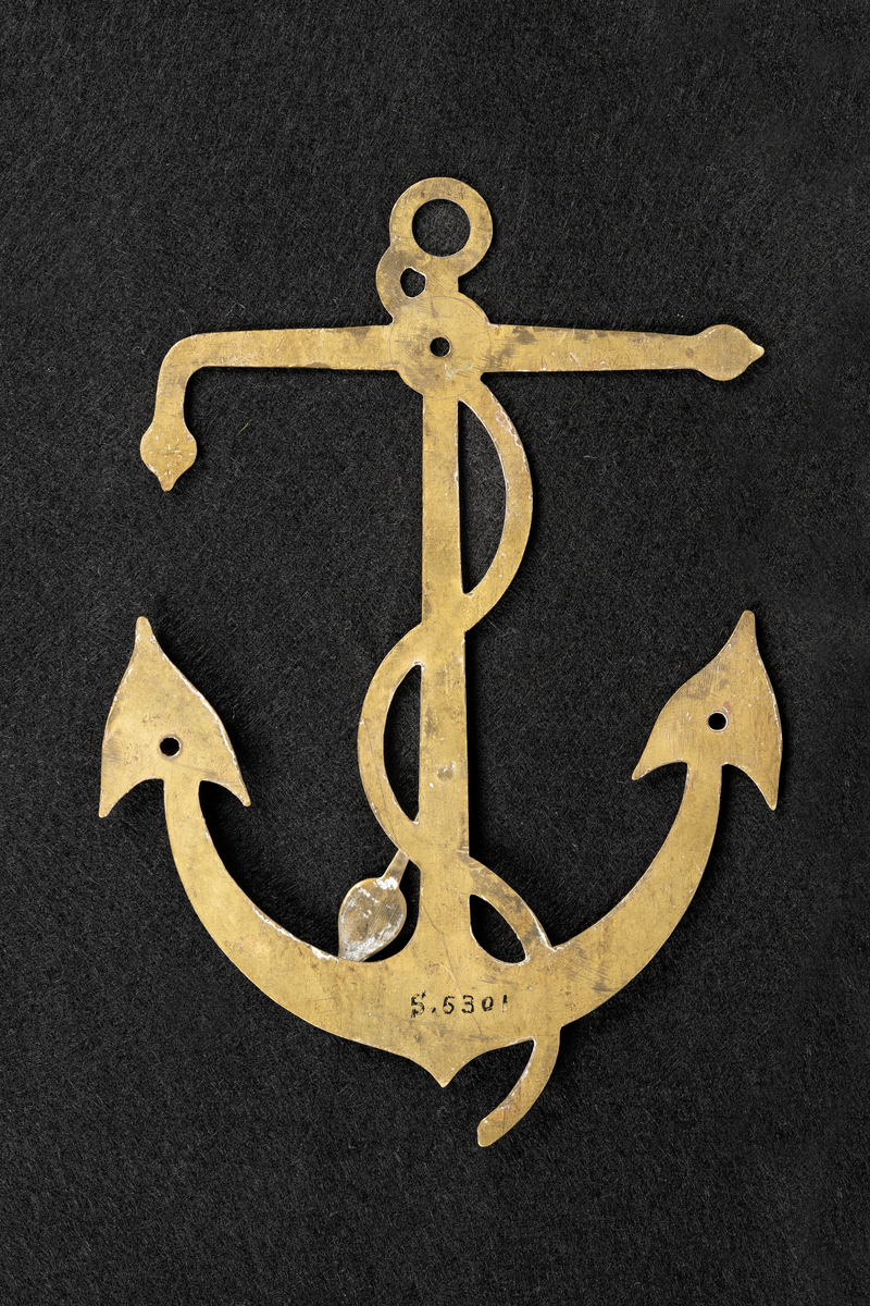 Regulator av mässing i form av ett ankare. Tillverkad i Reval av en maskinist ombord på FREJA 1888.