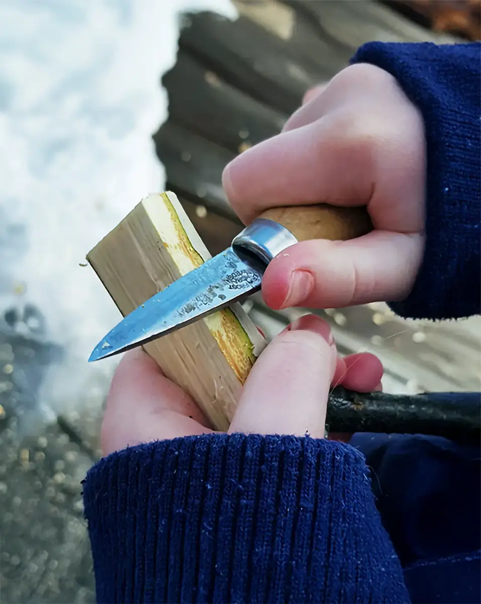 Barnhänder håller i en kniv mot en bit trä.