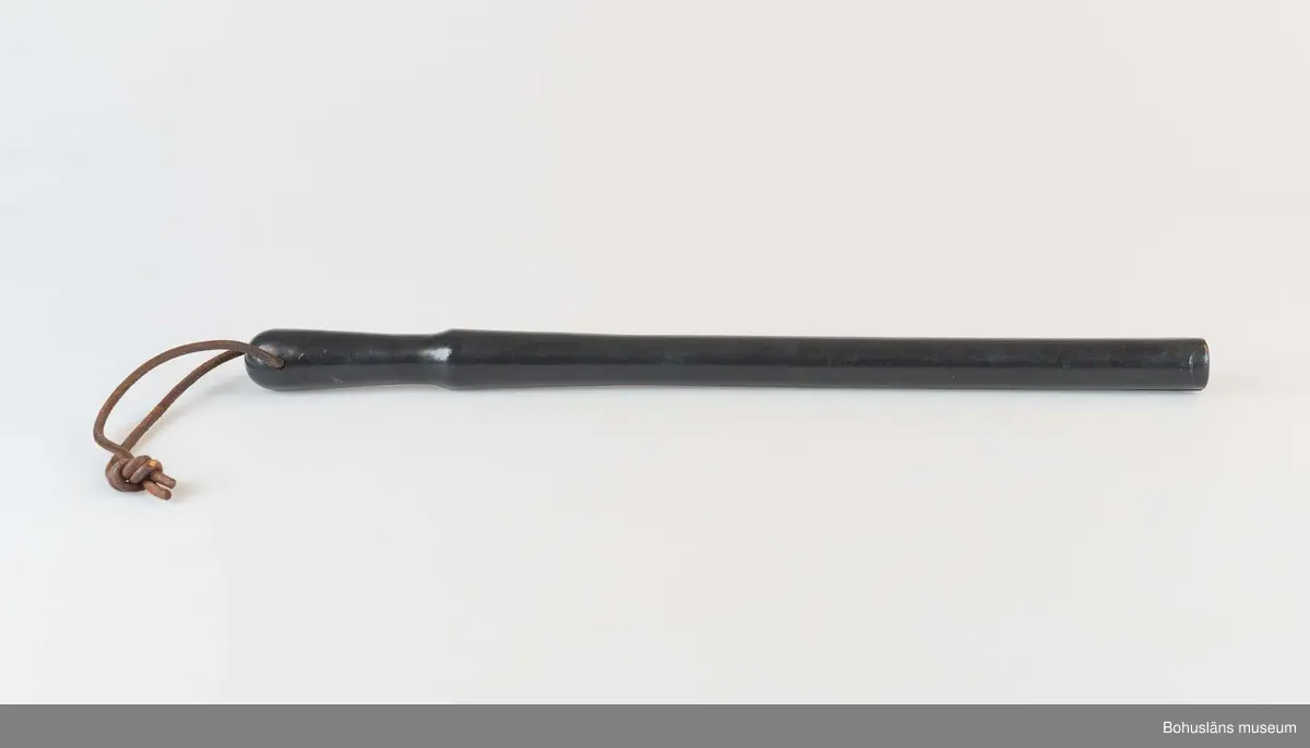 Svart gummibatong med lädersnöre. Batongen är utformad med handfäste och är avsmalnande nedåt. Handtaget är försett med hål för en läderrem som fästes runt handleden vid bärandet.

Batongen samhör med skinnjacka och mösskylt som använts i vakttjänstgöringen på  Uddevallavarvet.