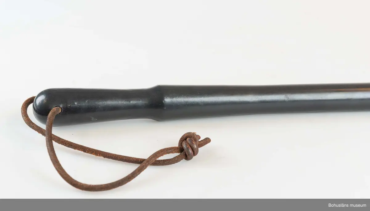 Svart gummibatong med lädersnöre. Batongen är utformad med handfäste och är avsmalnande nedåt. Handtaget är försett med hål för en läderrem som fästes runt handleden vid bärandet.

Batongen samhör med skinnjacka och mösskylt som använts i vakttjänstgöringen på  Uddevallavarvet.