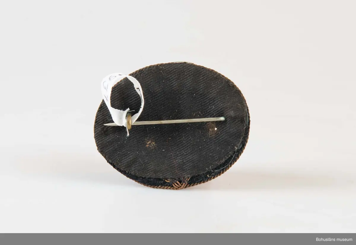 Ovalt och något välvt mössmärke med texten VAKT i förgyllda mässingsbokstäver på svart sammetsbotten. band runtom. På baksidan en kraftig nål med hyska.

Märket samhör med skinnjacka och batong som använts i vakttjänstgöringen på  Uddevallavarvet.