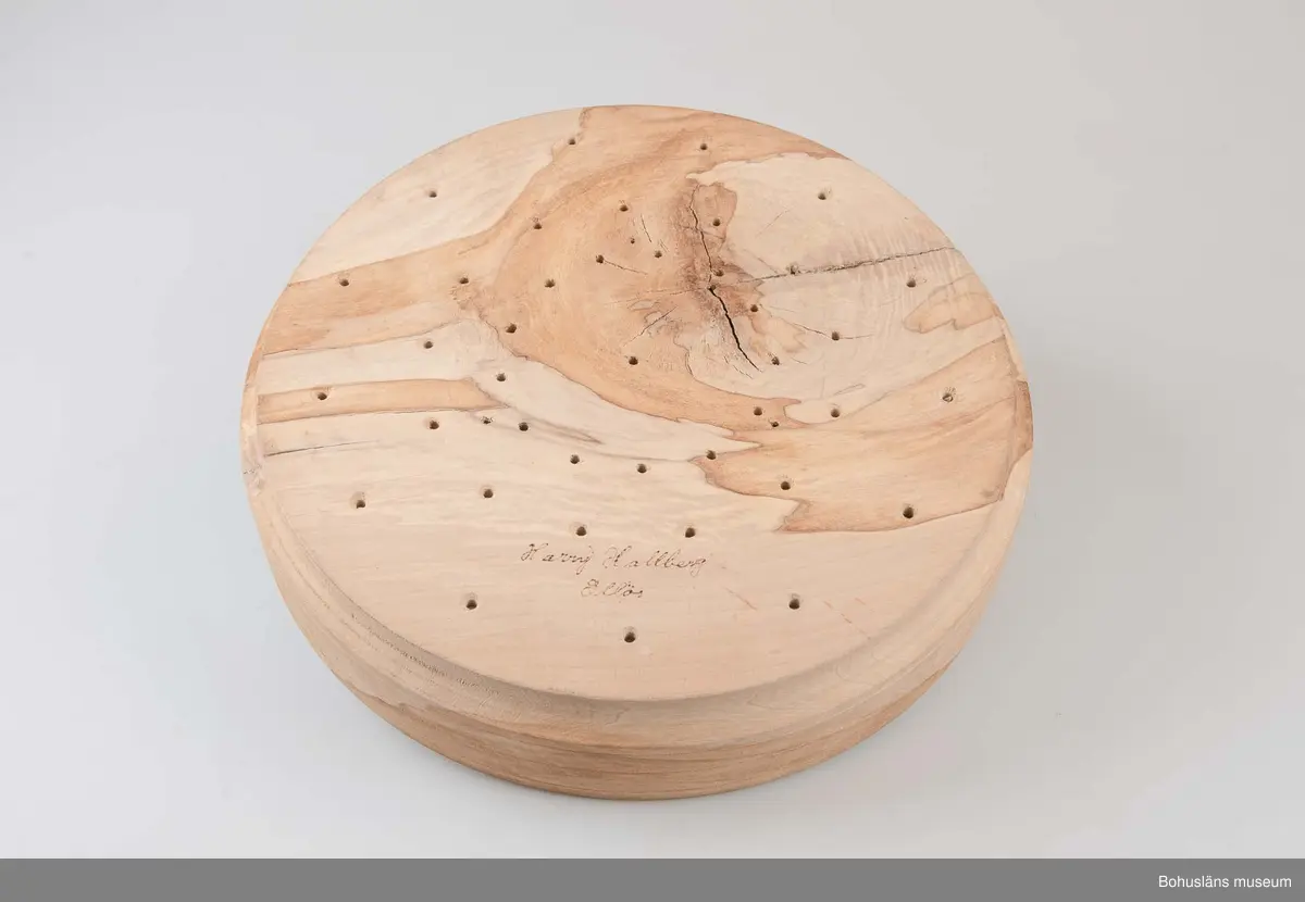 Rund, stor svarvad äggostform i lövträ med symmetriskt runda mönster och borrade hål. Utformad med hjälp av träborr av olika dimension. Linjedekor på utsidan.
På undersidan märkt med brännpenna: 
Harry Hallberg 
Ellös samt på sidan 
HH 1991.
Spricka.