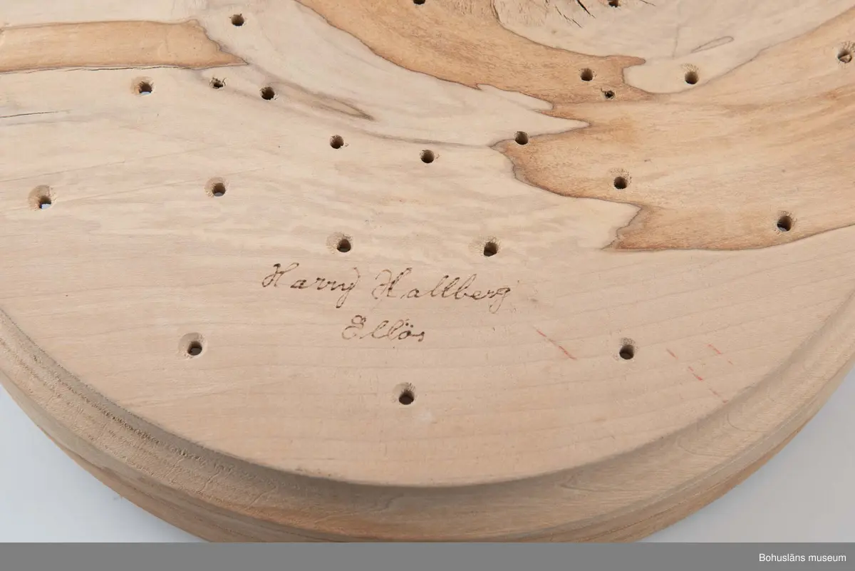 Rund, stor svarvad äggostform i lövträ med symmetriskt runda mönster och borrade hål. Utformad med hjälp av träborr av olika dimension. Linjedekor på utsidan.
På undersidan märkt med brännpenna: 
Harry Hallberg 
Ellös samt på sidan 
HH 1991.
Spricka.