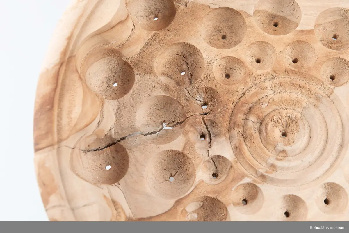 Rund, stor svarvad äggostform i lövträ med symmetriskt runda mönster och borrade hål. Utformad med hjälp av träborr av olika dimension. Linjedekor på utsidan.
På undersidan märkt med brännpenna: 
Harry Hallberg 
Ellös samt på sidan 
HH 1991.
Spricka.