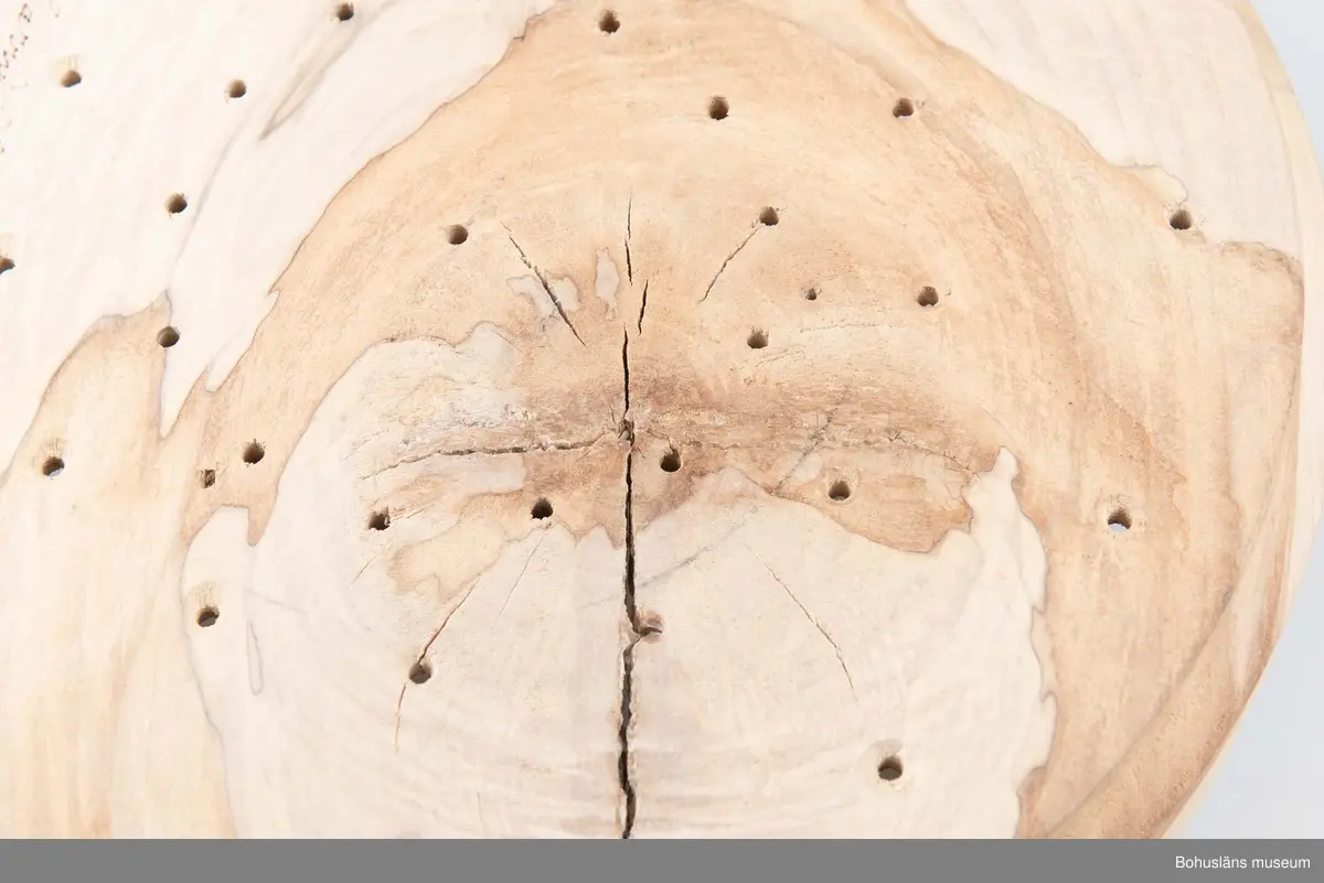 Rund, stor svarvad äggostform i lövträ med symmetriskt runda mönster och borrade hål. Utformad med hjälp av träborr av olika dimension. Linjedekor på utsidan.
På undersidan märkt med brännpenna: 
Harry Hallberg 
Ellös samt på sidan 
HH 1991.
Spricka.