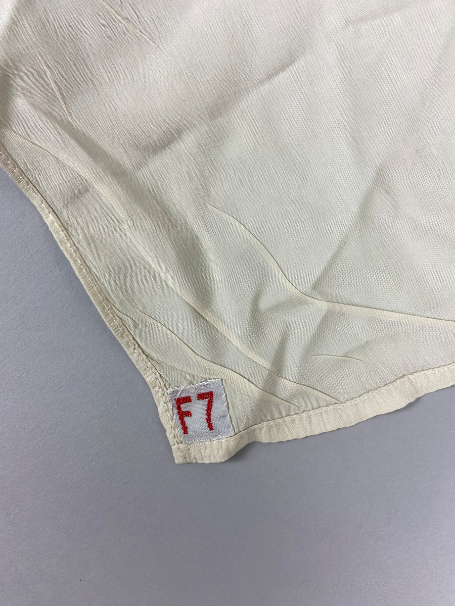 Flyghalsduk i siden, långsmal, vit, maskinsydd smal fåll. Användes av flyglärare, stabsflygare och övriga. Påsydd vävd etikett "F 7".