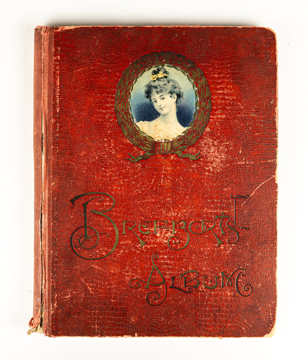 Fotoalbum med röda pärmar, guldfärgad text "Brefkortsalbum" samt bild på ett kvinnoansikte omgivet av en guldfärgad krans.