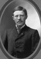 Studioportrett av mann kledd i dress, vest, hvit skjorte og 