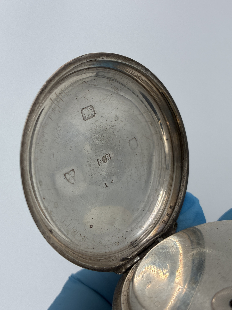 Fickur med vitemaljerad urtavla med romerska siffror och separat sekundvisare.
Text på urtavlan: "The Climax Trip Action Patent H. SAMUEL MANCHESTER".

Boett av silver med engelska stämplar
Lejon = England 
H.S = Okänd mästare 
Vapen med svärd och tre vetekärvar = Chester 
Otydbar årsstämpel

Kedja av mässing. Kedjans längd: ca 33 cm.