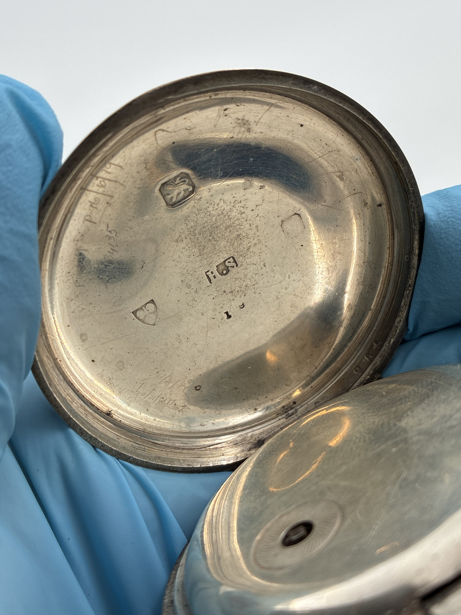 Fickur med vitemaljerad urtavla med romerska siffror och separat sekundvisare.
Text på urtavlan: "The Climax Trip Action Patent H. SAMUEL MANCHESTER".

Boett av silver med engelska stämplar
Lejon = England 
H.S = Okänd mästare 
Vapen med svärd och tre vetekärvar = Chester 
Otydbar årsstämpel

Kedja av mässing. Kedjans längd: ca 33 cm.