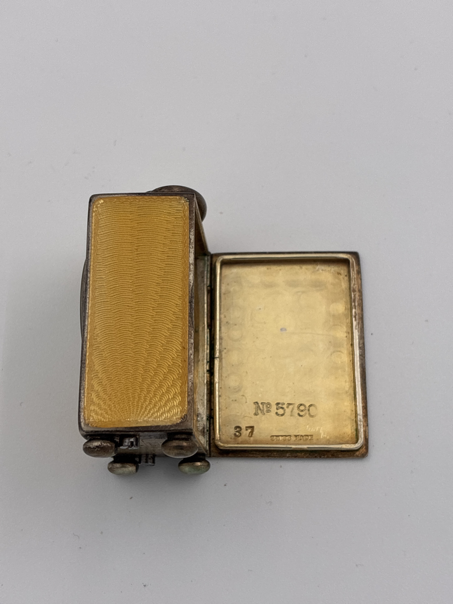 Reseur med fodral och nyckel. Rektangulär form. Boett av silver, på fyra sidor försedd med gul emalj.
Urverkets tillverkningsnummer: 162038
Boetten upptill med ögla, står på fyra runda fötter.
Fodral av läder.

Storlek: Uret: 2,9 x 1,8 x 3,7 cm.
              Fodralet: 4,3 x 4,0 x 6,0 cm.

Modell/Fabrikat/typ: Zenith