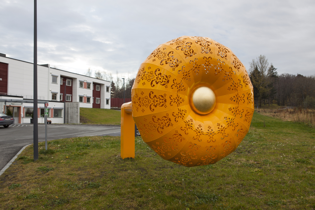 Gul skulptur formet som en trakt, en tut, med kniplingemønter utskjært i overflaten. 