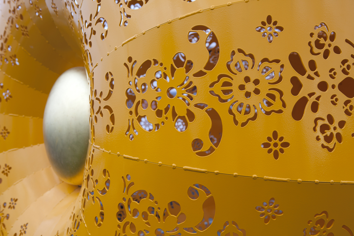 Gul skulptur formet som en trakt, en tut, med kniplingemønter utskjært i overflaten. 