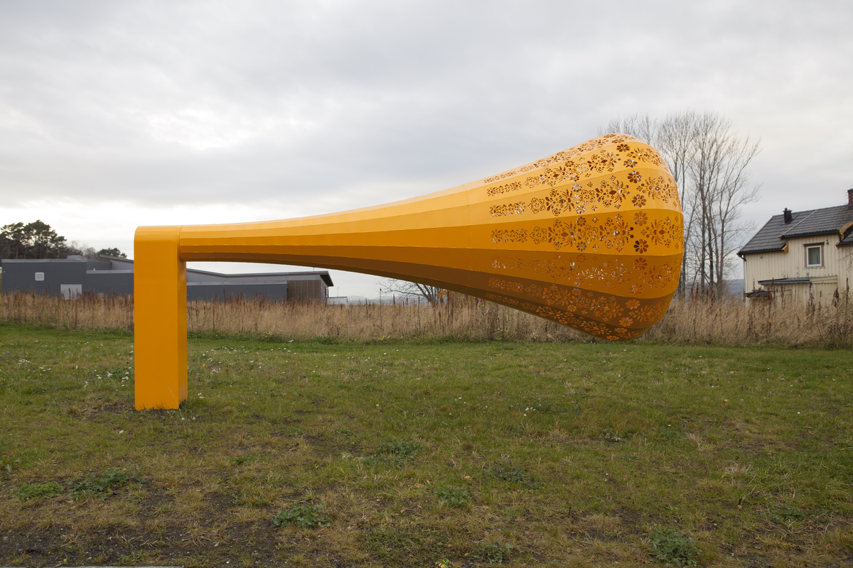 Gul skulptur formet som en trakt, en tut, med kniplingemønter utskjært i overflaten. 