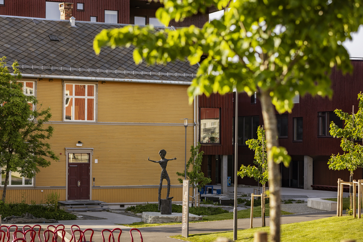 En gutt som balanserer på ett bein på en stubbe. En fot er kort, den andre er lang, armene er strekt forover. Figuren har mange ansikter, flere på baksiden. 