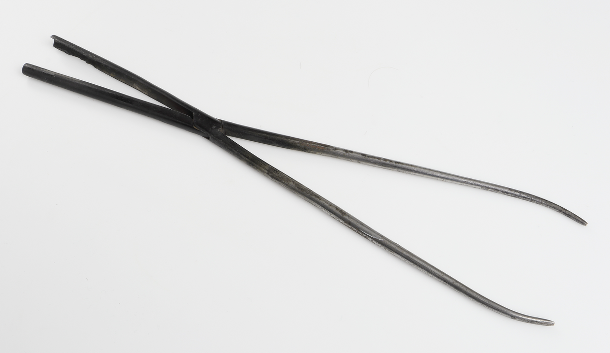 Locktång av metall. Raka skänklar, den ena rund, den andra formad som en ränna. 

Inskrivet i huvudbok år 1955.