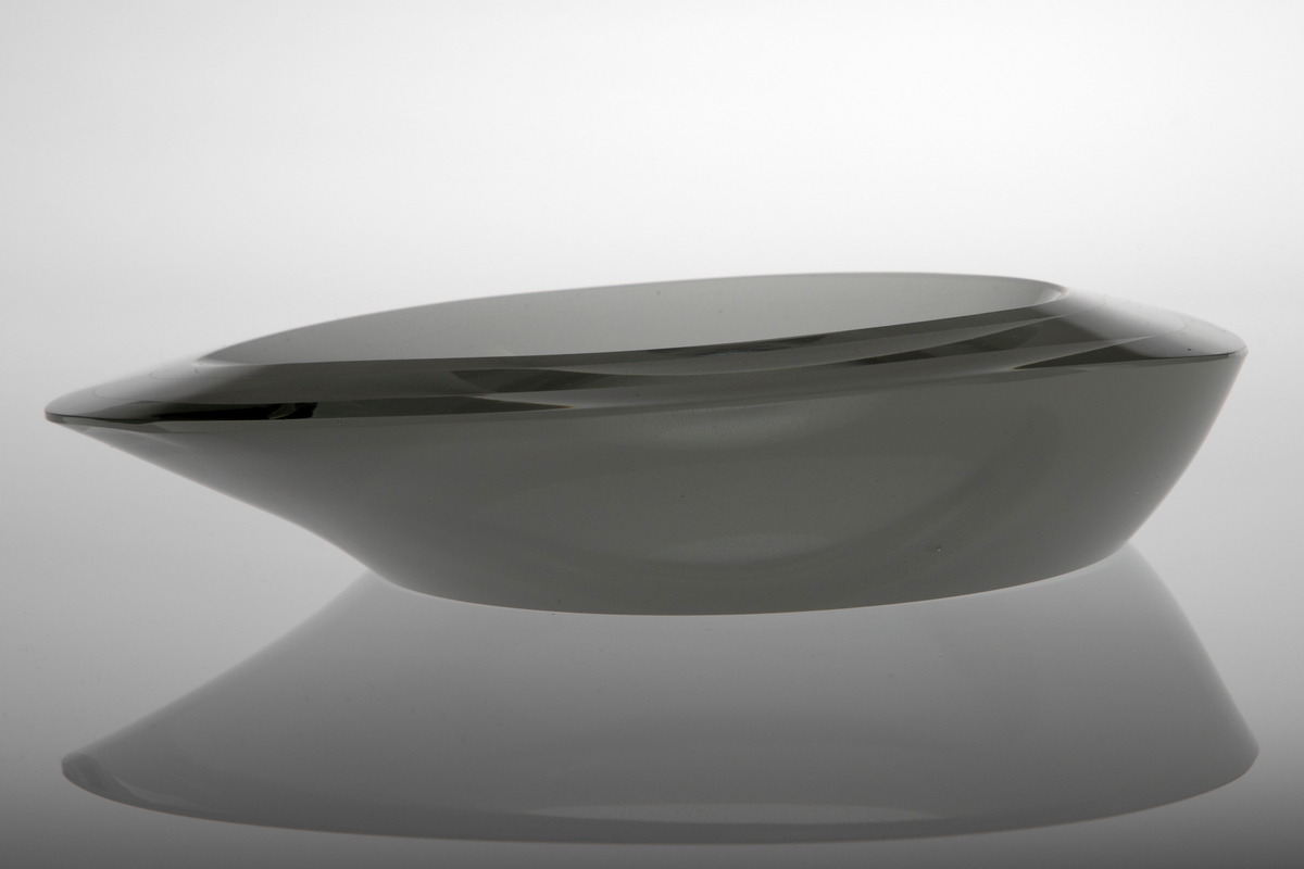 Askebeger i overfangsglass. Oval form med tilspisning i en side og en lav fordypning i midten. Sammensatt av tre tykke parallelle lag klart glass med matte mellomvegger. Lagene er skrådd inn mot bunnflaten og gir den midtre fordypningen sin form. Bunnflaten er dekorert med konsentriske ringer i variert matthetsgrad.