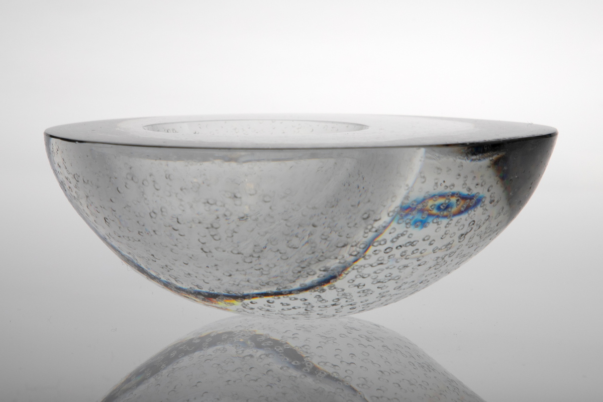 Askebeger i klart glass. Halvkuleformet med noe uregelmessig rund form øverst. Avrundet bunnflate. På overflaten en mindre halvkuleformet fordypning, plassert noe bort fra flatens sentrum. Utsiden er etterbehandlet med punsling.