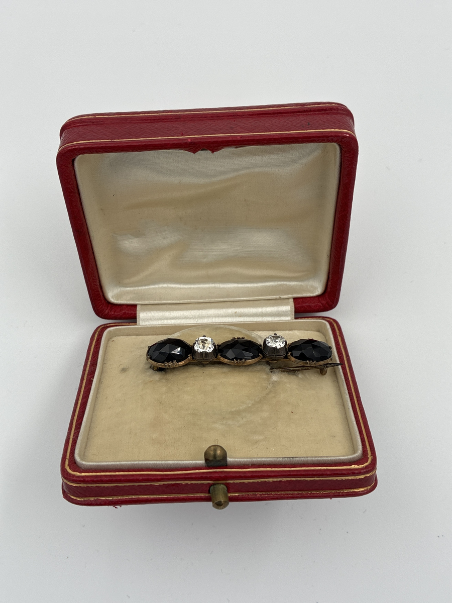 Tre svarta stanar, troligen gagat eller onyx, och två vita stenar i infattning av förgyllt silver.

Stämplar: Trekronorsstämpel
Årsbokstav: K7 (1912)
Stadsstämpel: oläslig, troligen Stockholm
Mästarstämpel " I SUNDSTRÖM" = Israel Sundström

I etui, troligen inte original till broschen, med krönt monogram C.A = Claes Adelsköld.