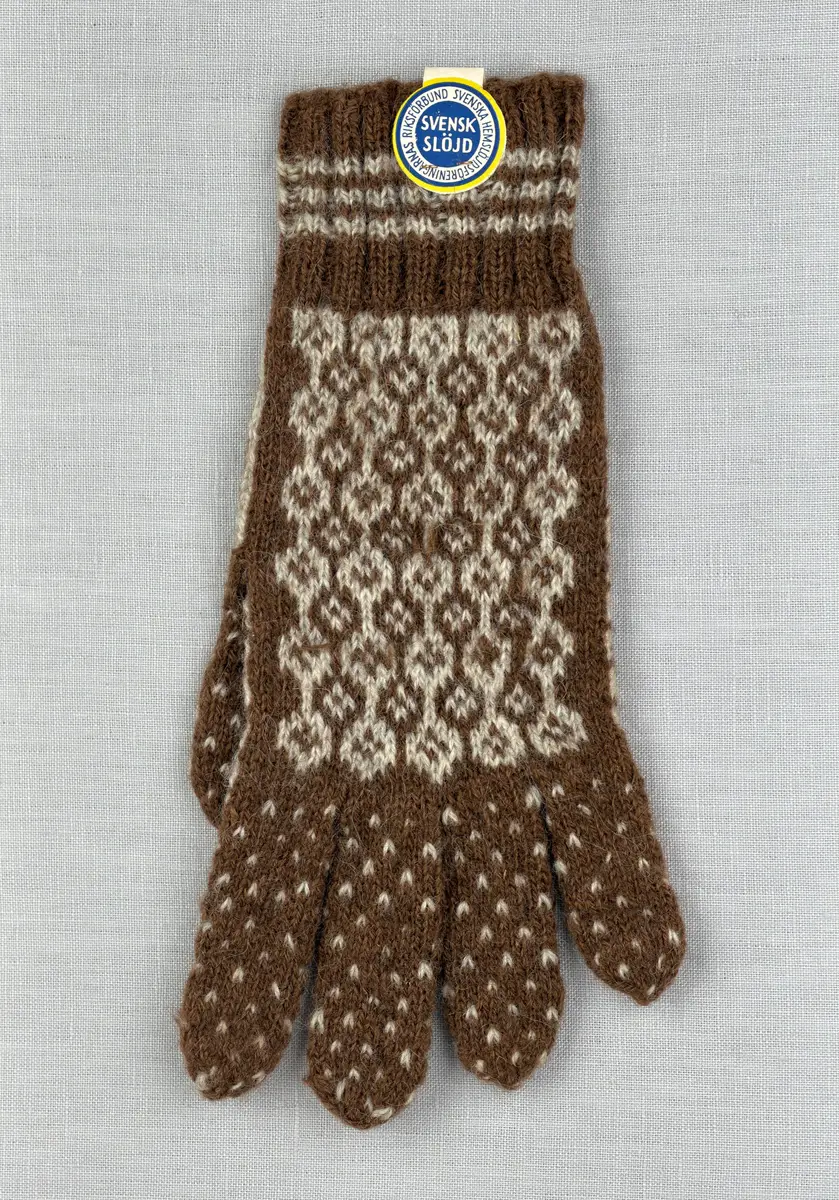 En stickad fingervante, med randig mudd i 2-2 resår (2 räta och 2 aviga maskor) och mönsterstickad vante i slätstickning, av 2-trådigt ullgarn.