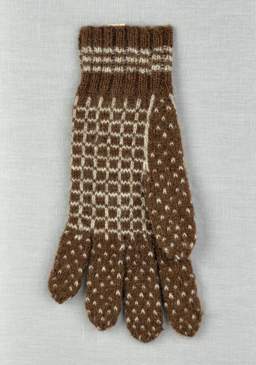 En stickad fingervante, med randig mudd i 2-2 resår (2 räta och 2 aviga maskor) och mönsterstickad vante i slätstickning, av 2-trådigt ullgarn.