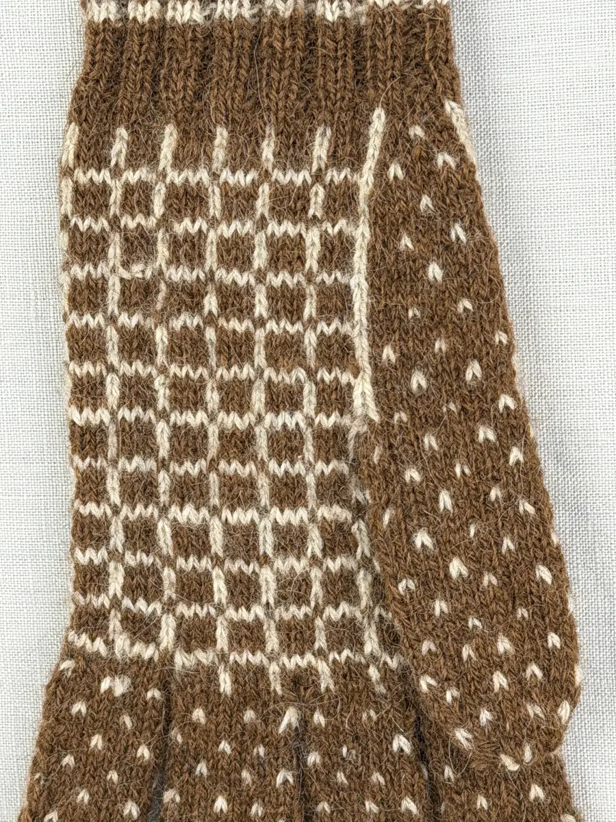 En stickad fingervante, med randig mudd i 2-2 resår (2 räta och 2 aviga maskor) och mönsterstickad vante i slätstickning, av 2-trådigt ullgarn.