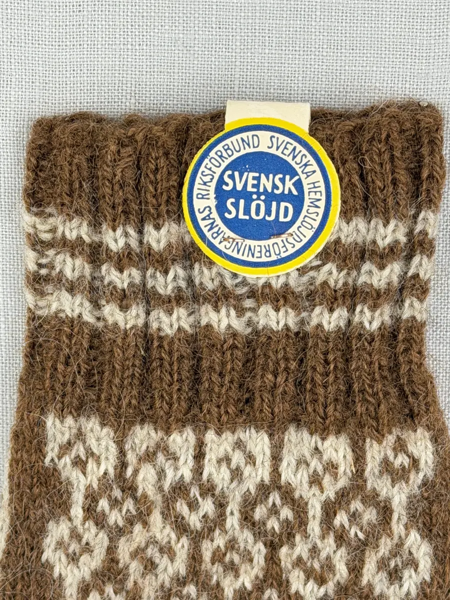 En stickad fingervante, med randig mudd i 2-2 resår (2 räta och 2 aviga maskor) och mönsterstickad vante i slätstickning, av 2-trådigt ullgarn.