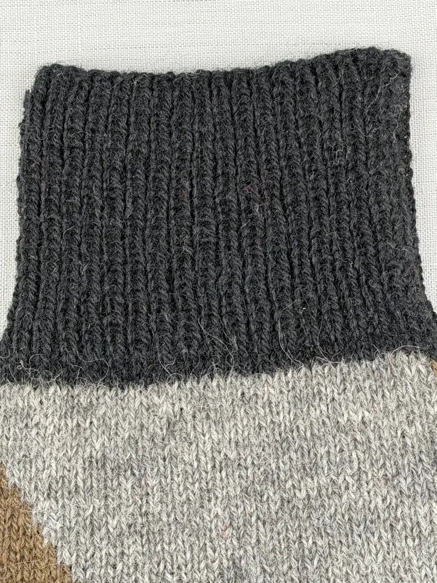 En stickad socka, med mudd i 1-1 resår (1 rät och 1 avig maska), skaft mönstrat med intarsia och fot i slätstickning, av 2-trådigt ullgarn.
