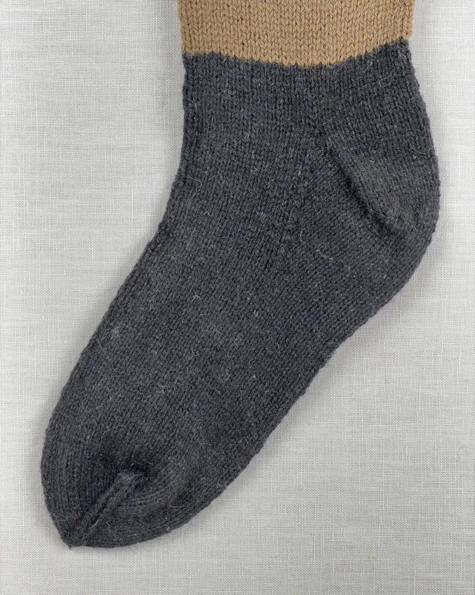 En stickad socka, med mudd i 1-1 resår (1 rät och 1 avig maska), skaft mönstrat med intarsia och fot i slätstickning, av 2-trådigt ullgarn.
