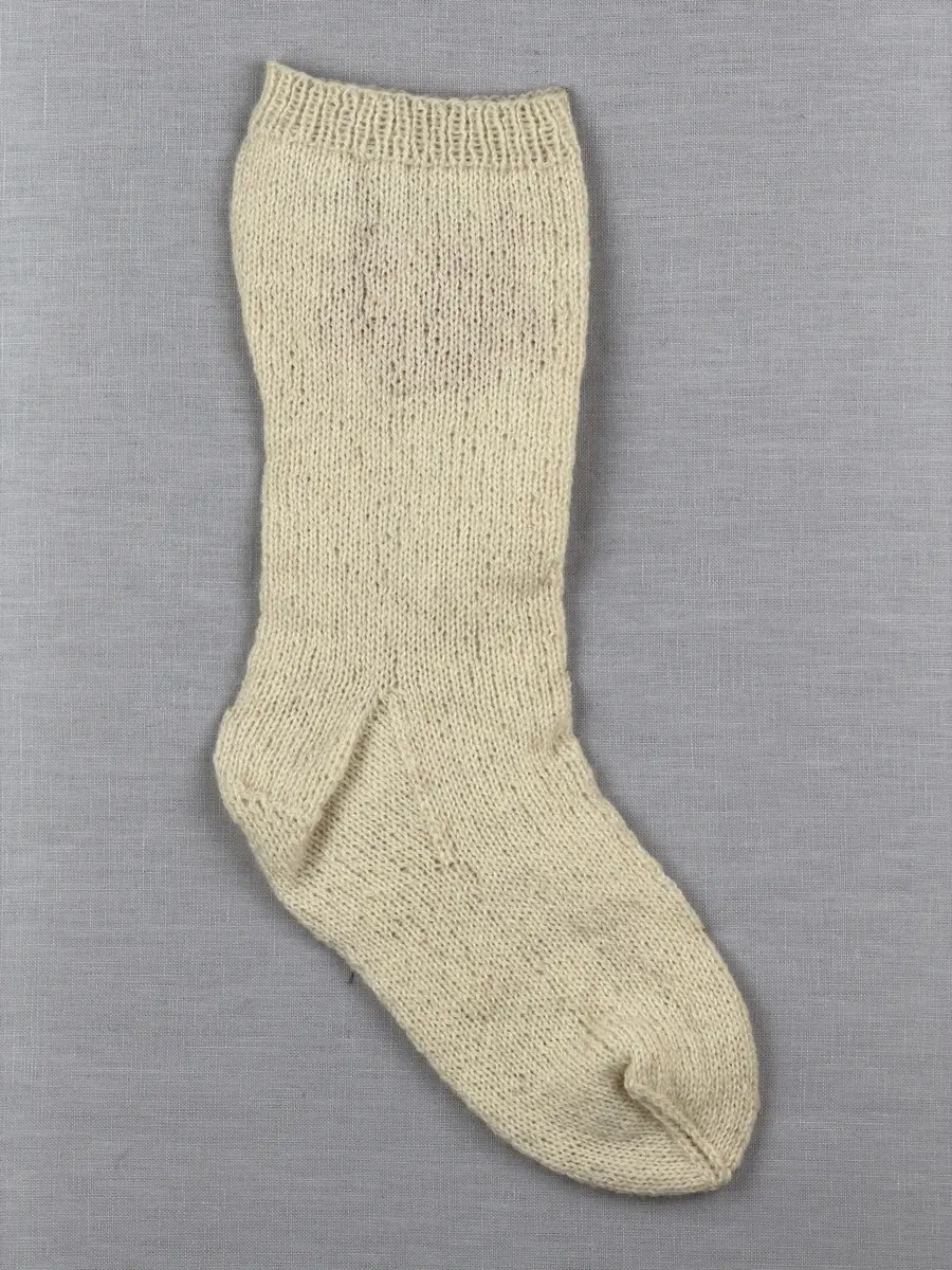 En stickad socka, med mudd i 1-1 resår (1 rät och 1 avig maska) och skaft och fot i slätstickning av 2-trådigt ullgarn. Sockans skaft är dekorerad på yttersidan med ett ullgarns broderi i maskstygn.
