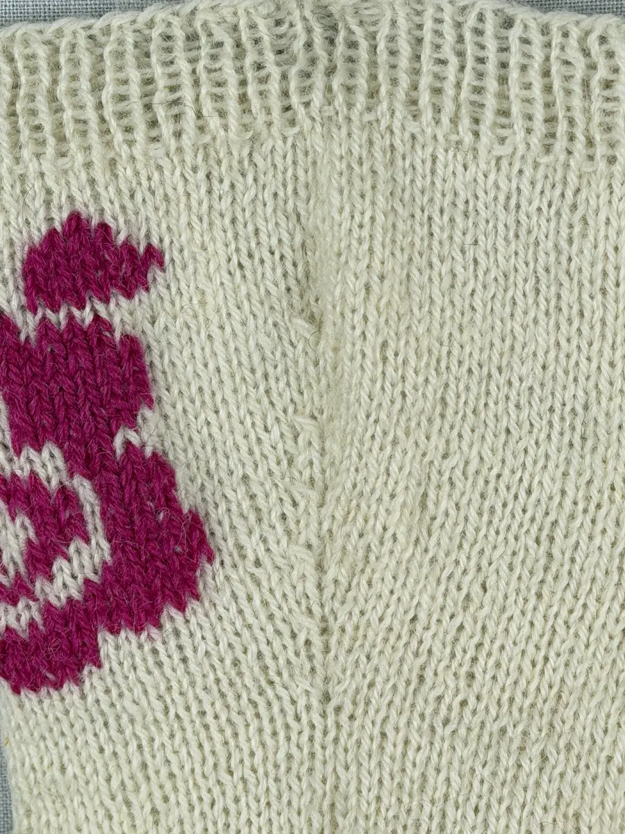 En stickad socka, med mudd i 1-1 resår (1 rät och 1 avig maska) och skaft och fot i slätstickning av 2-trådigt ullgarn. Sockans skaft är dekorerad på yttersidan med ett ullgarns broderi i maskstygn.
