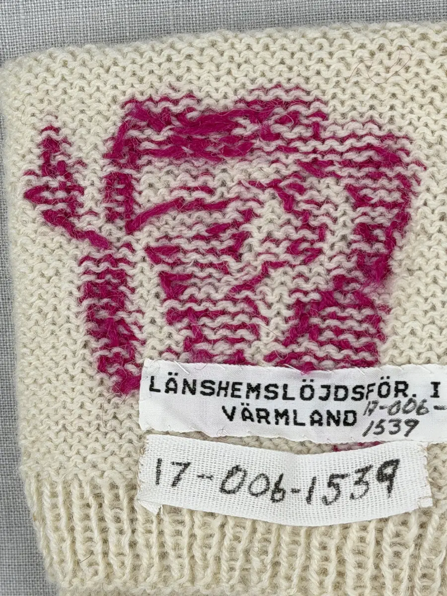 En stickad socka, med mudd i 1-1 resår (1 rät och 1 avig maska) och skaft och fot i slätstickning av 2-trådigt ullgarn. Sockans skaft är dekorerad på yttersidan med ett ullgarns broderi i maskstygn.
