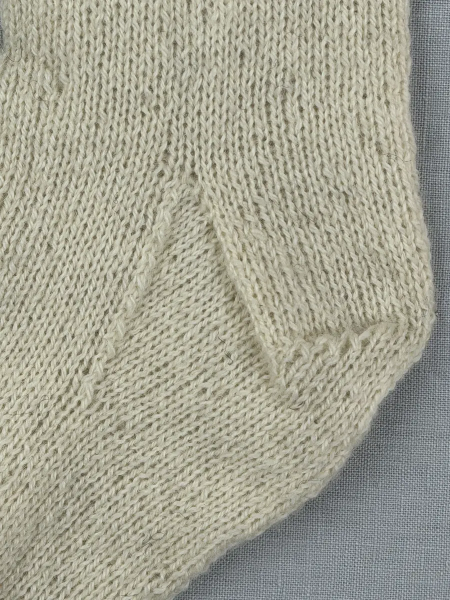 En stickad socka, med mudd i 1-1 resår (1 rät och 1 avig maska) och skaft och fot i slätstickning av 2-trådigt ullgarn. Sockans skaft är dekorerad på yttersidan med ett ullgarns broderi i maskstygn.
