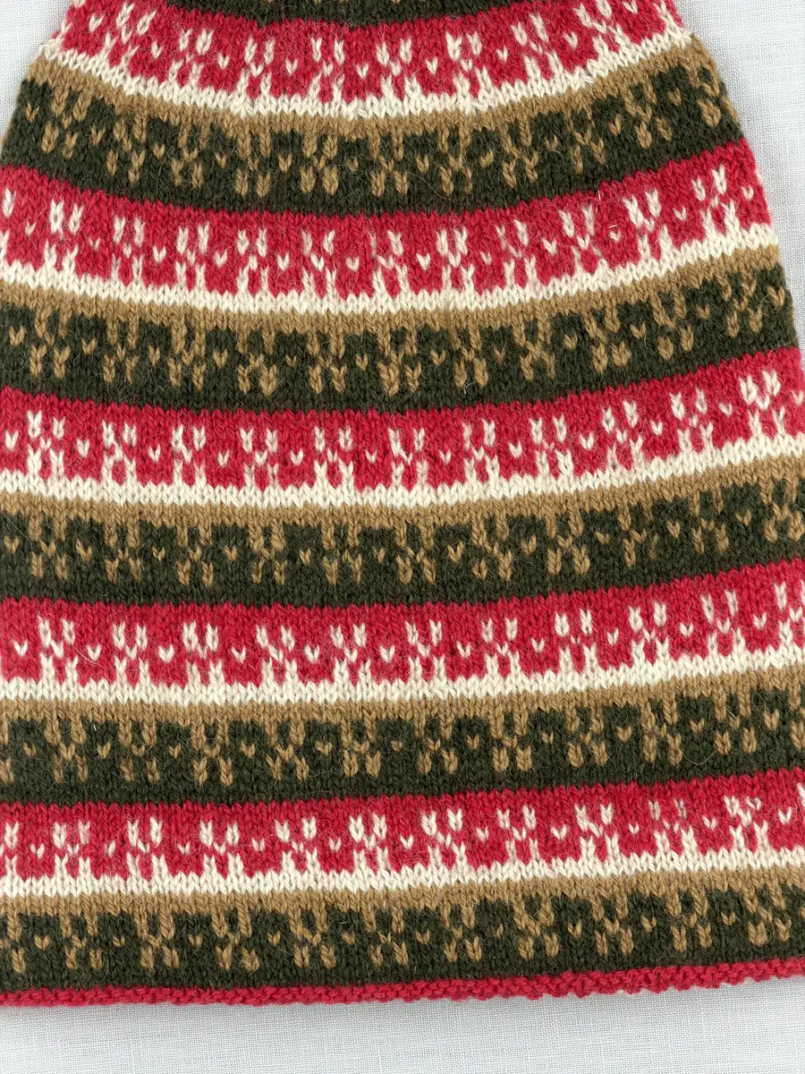 En stickad mössa, i mönsterstickad slätstickning, av 2-trådigt ullgarn. Mössan är rundstickad och har en fåll med 1-1 resår (1 rät och 1 avig maska) i nederkant, som är fastsydd med kaststygn. Toppen på mössan är formad med strålhoptagning och högst upp sitter en tofs fastsatt med en påtad snodd.
